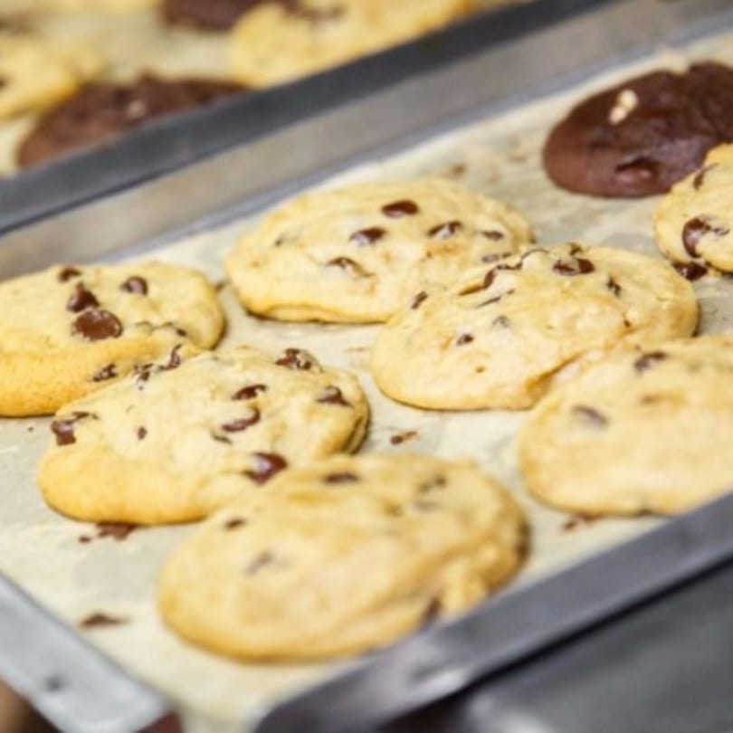 Freshly baked chocolate chip cookies and a few double chocolate cookies on a baking sheet.