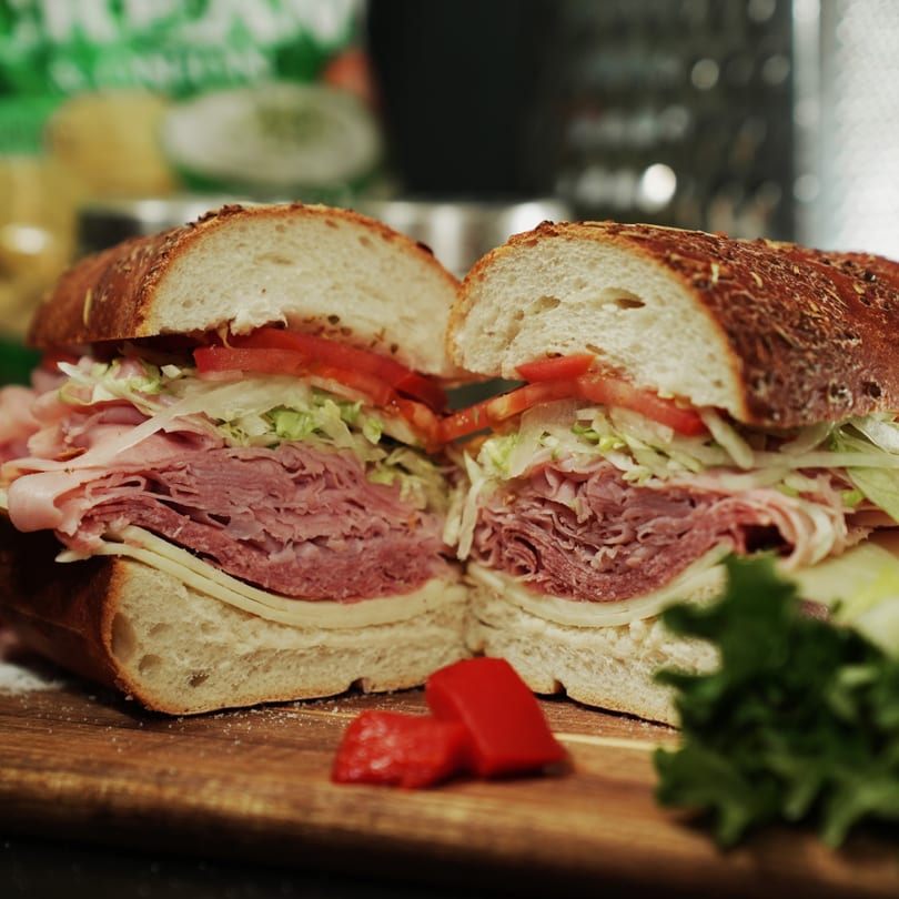 A large Great Wazu sandwich, cut in half, revealing layers of meat, cheese, lettuce, and tomatoes.