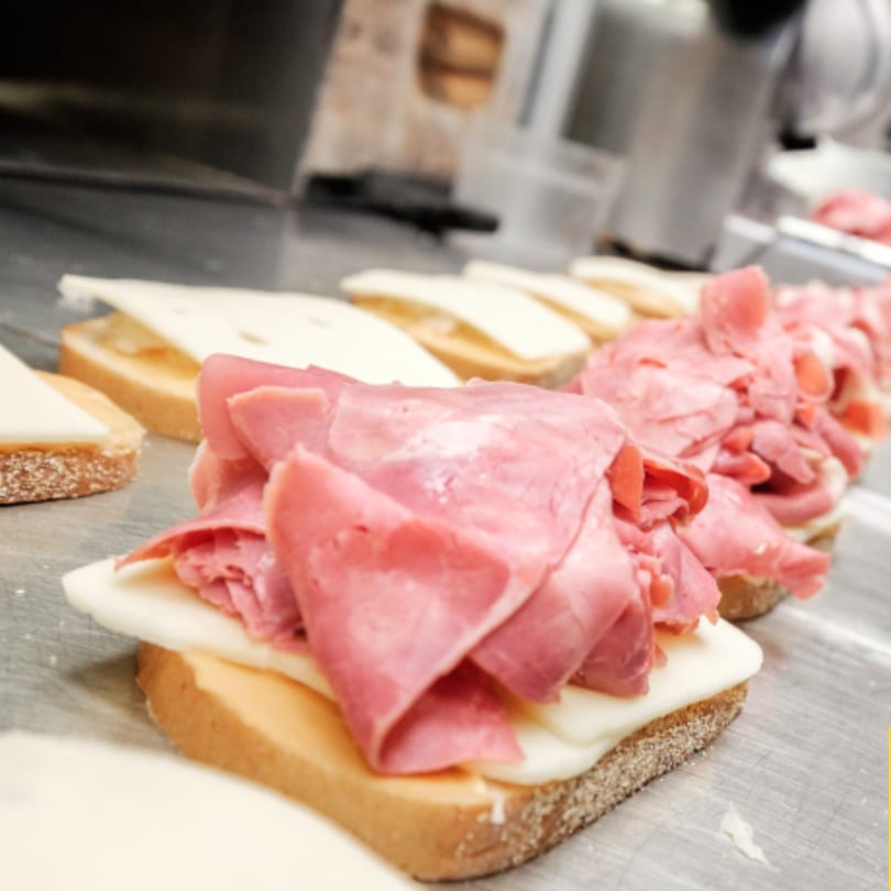 A row of open-faced sandwiches with cheese and thinly sliced roast beef on a metal counter.
